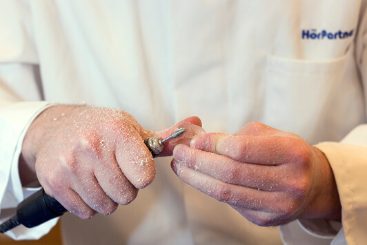 Ein Hörakustiker bearbeitet ein Hörgerät handwerklich zur individuellen Anpassung.